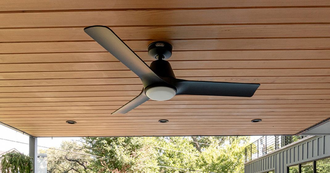 Black three-blade ceiling fan installed beneath a covered outdoor living space with a warm wood-plank ceiling.
