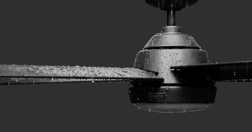 Close-up of a black Hunter outdoor ceiling fan covered in water droplets, demonstrating exposure to wet conditions.
