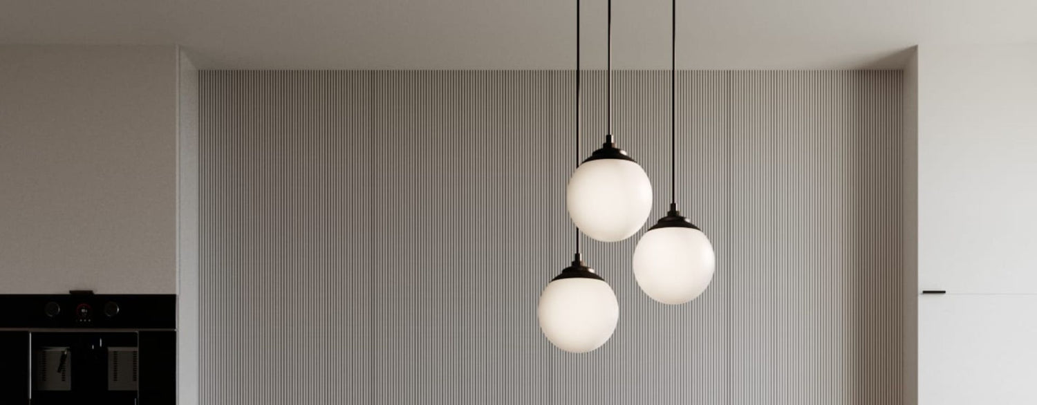 Three hanging globe pendant lights with black fixtures illuminate a sleek kitchen with textured wall paneling and clean cabinetry.