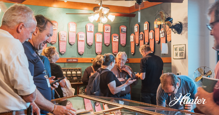 Visitors gathered around a display case in a museum-style space, exploring historical Hunter fans and archival exhibits.
