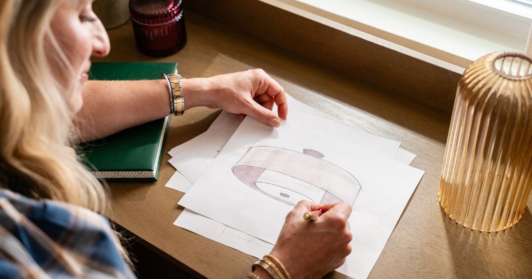 Close-up lifestyle image of a designer sketching a lighting concept at a desk beside a warm amber table lamp.