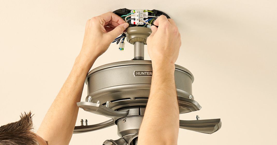 Close-up of a person connecting electrical wiring during the installation of a Hunter ceiling fan.