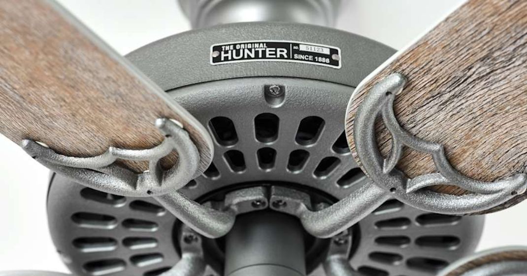 Close-up underside view of a Hunter Original ceiling fan featuring wood-finish blades, decorative cast-metal blade irons, vented motor housing, and the “Original Hunter Since 1886” nameplate.