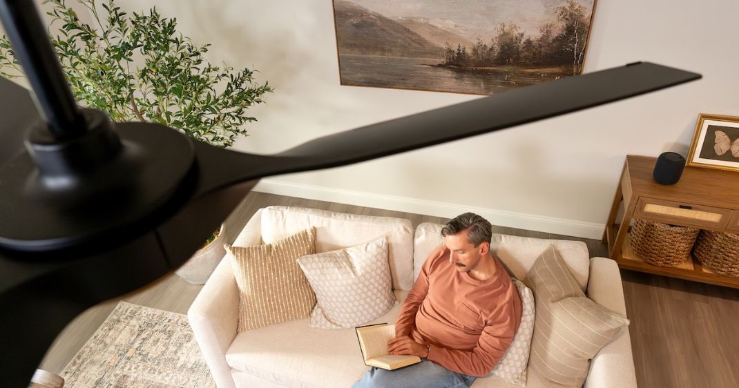 Overhead lifestyle view of a black ceiling fan above a living room, with a person reading on a sofa below.
