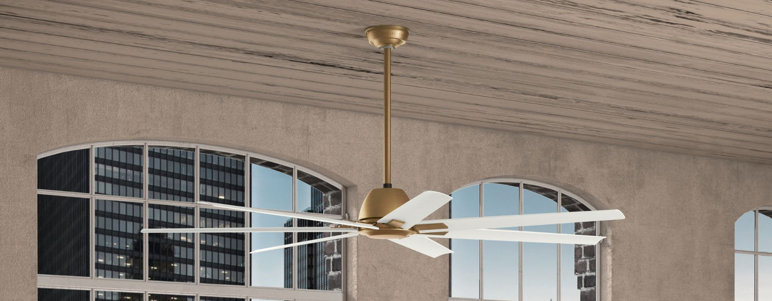 Large modern ceiling fan with multiple white blades and a brushed gold motor housing, suspended from a downrod in a space with arched windows and a textured ceiling