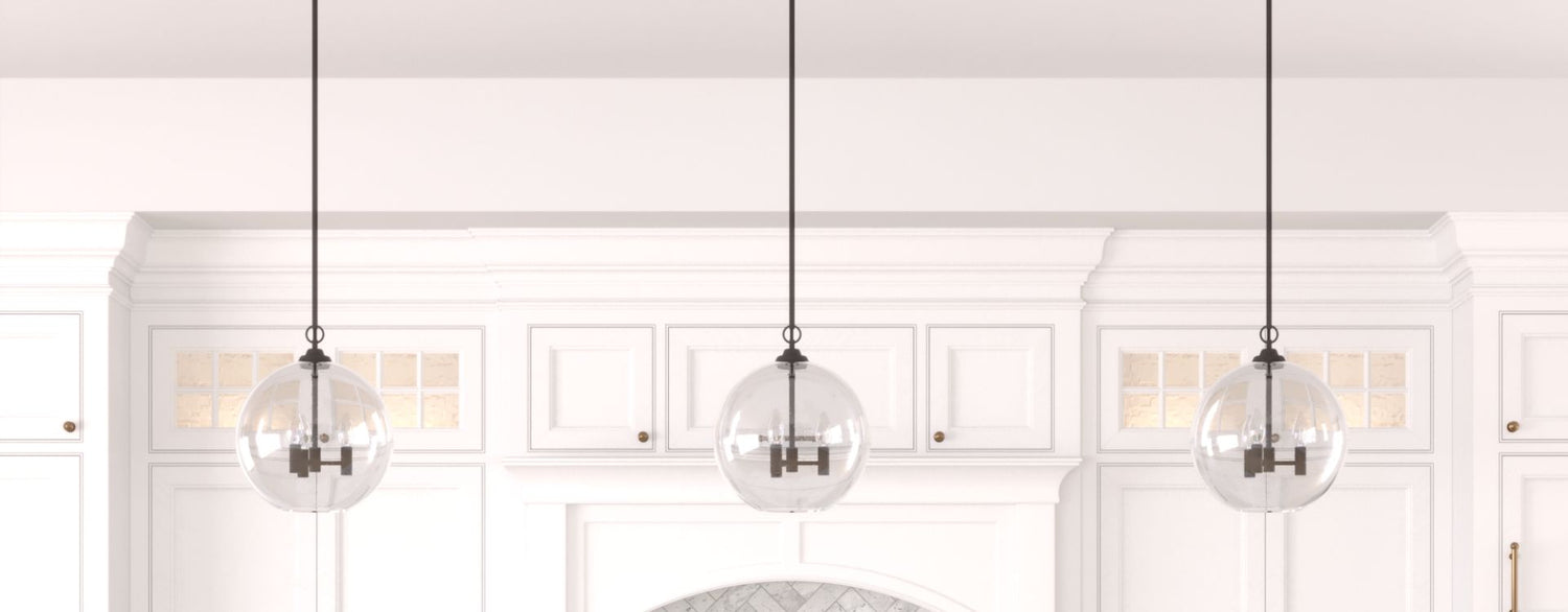 Three evenly spaced glass globe pendant lights hang above a bright kitchen, complementing white cabinetry and classic architectural details.