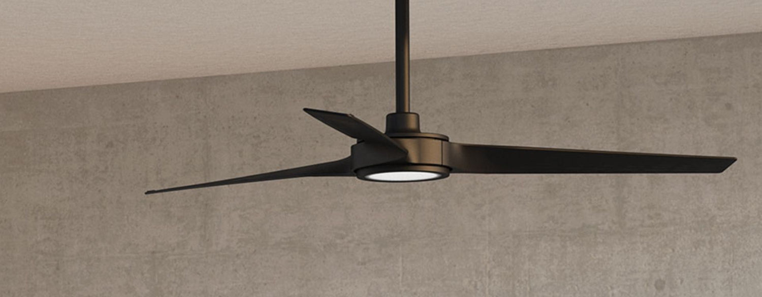Modern black three-blade ceiling fan with integrated LED light mounted on a downrod, set against a smooth concrete wall in a contemporary interior
