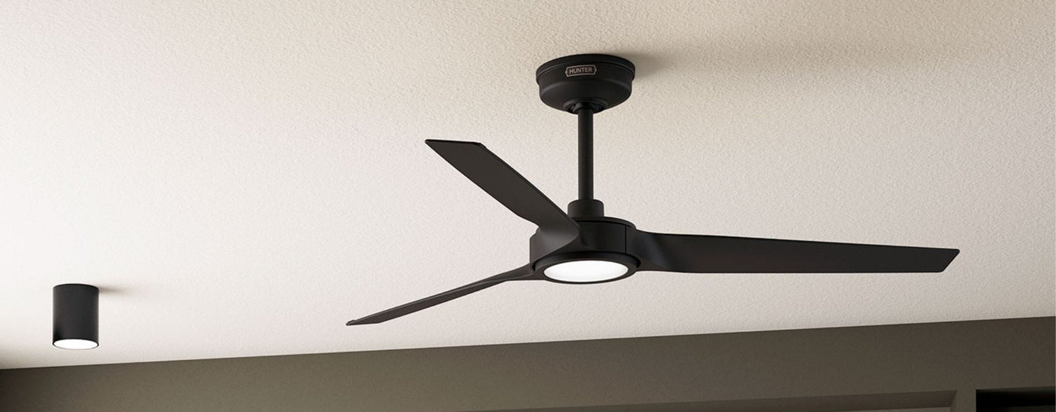 Modern black three-blade ceiling fan with integrated LED light mounted on a downrod, installed on a textured ceiling in a contemporary interior