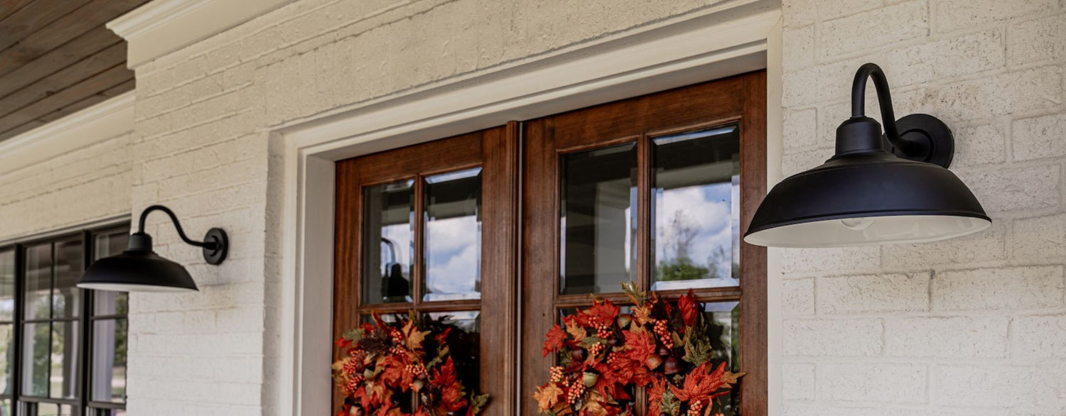 Exterior home entrance featuring black barn-style wall lights, wooden double doors, and fall wreath accents.